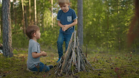 Two-boys-brothers-3-6-years-old-in-the-forest-collect-and-set-up-campfire-sticks-at-sunset-during-a-family-camping-trip